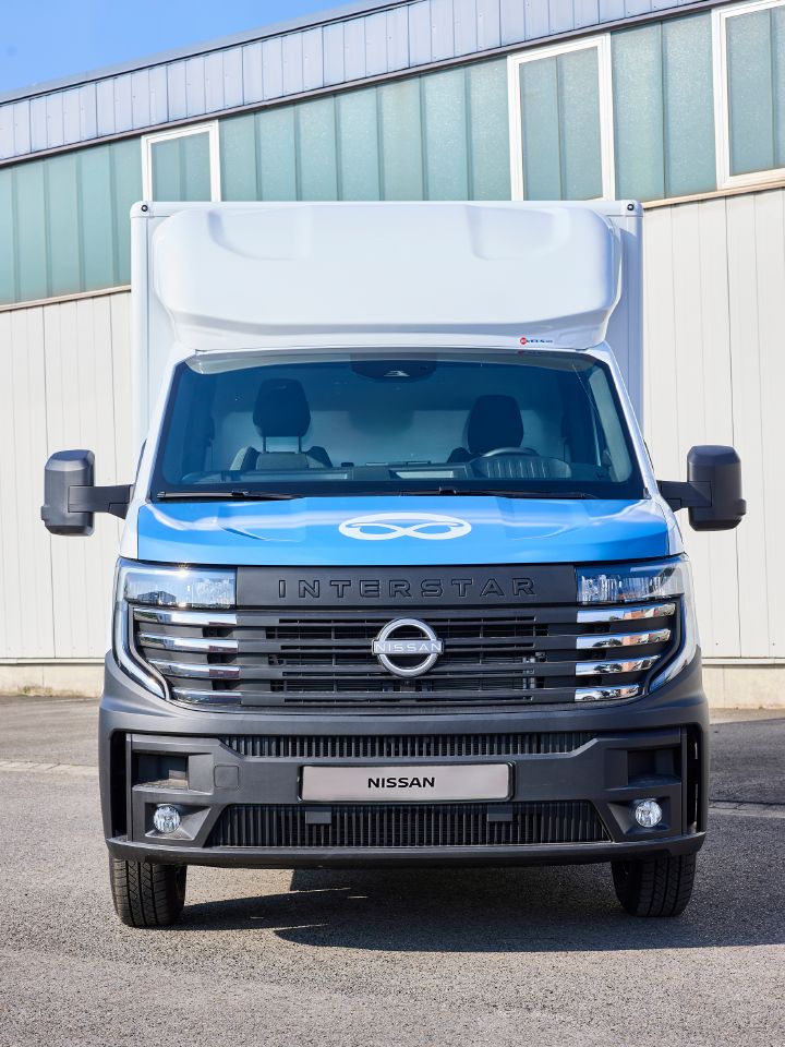 Statische Frontaufnahme des Nissan Interstar-e mit Bäckereikoffer, auf der blauen Motorhaube ist eine weiße Brezel abgebildet