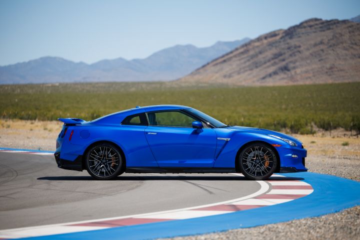 Profile of a blue 2024 Nissan GT‑R Special Edition parked at a turn of a race track with a mountain and sky in the background