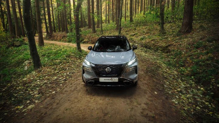 Vogelperspektive auf einen grauen Nissan X‑Trail N-Trek, der offroad durch den Wald fährt
