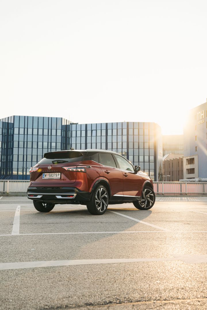 Blick von schräg hinten auf einen parkenden Nissan Qashqai in Fuji Sunset Red im Sonnenuntergang