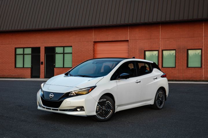Front left 3/4 view of a white 2025 Nissan LEAF in front of a red brick building.