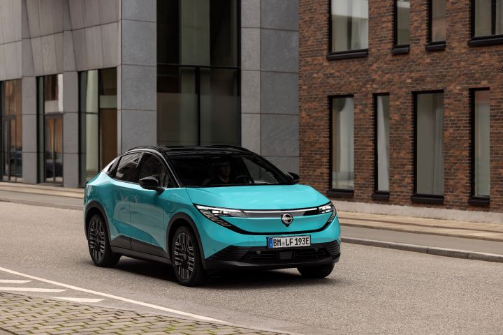 3/4 Frontaufnahme eines türkisen Nissan LEAF, der auf einer Straße vor einem modernen Gebäude mit Backstein- und Glas-Fassade steht