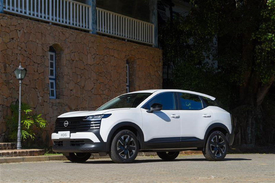 SUV Nissan Kicks branco estacionado em rua de paralelepípedos, em frente a prédio com paredes de pedra e janelas em arco