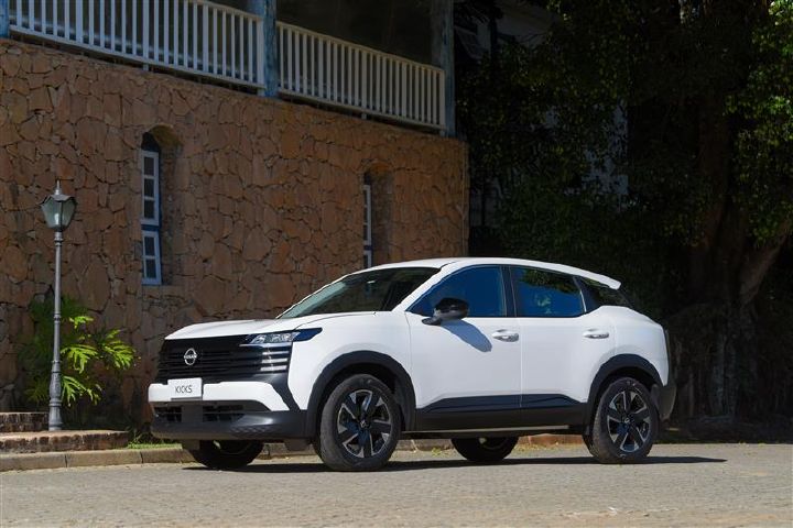 SUV Nissan Kicks branco estacionado em rua de paralelepípedos, em frente a prédio com paredes de pedra e janelas em arco
