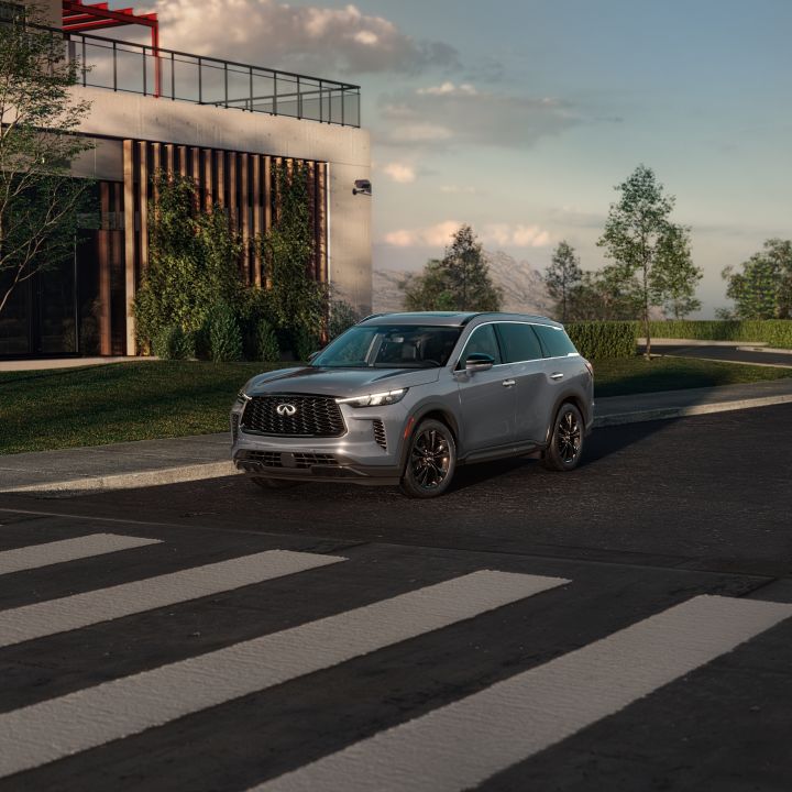 Front left 3/4 view of a 2025 INFINITI QX60 parked in front of a white modern building with blue skies behind.