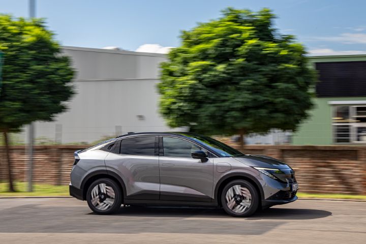 Vor einer halbhohen, roten Backsteinmauer fährt seitlich ein grauer Nissan Leaf