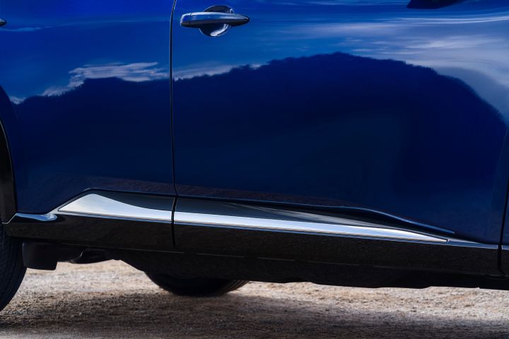 Nissan X‑Trail Tekna in der Karosseriefarbe Universal Blue mit Nahaufnahme der Seitentür und der unteren Karosserieverkleidung mit silbernen Zierleisten. Das Bild hebt die glänzende Lackierung und die eleganten Designelemente des Fahrzeugs vor einem neutralen Hintergrund hervor.