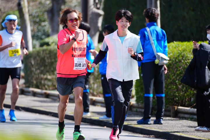 赤いシャツを着た高橋勇市さんと、日産ロゴ入りの白いベストを着た男性が走る様子