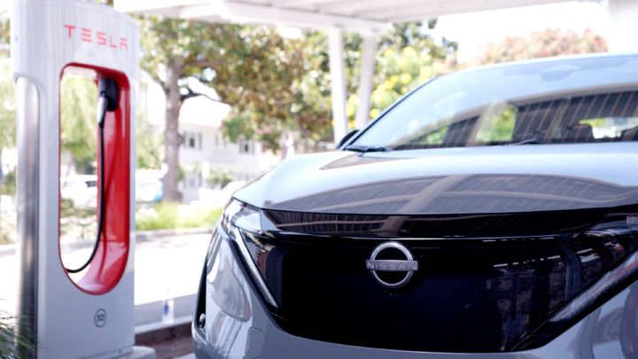 A gray Nissan Ariya parked by Tesla supercharger outdoors.