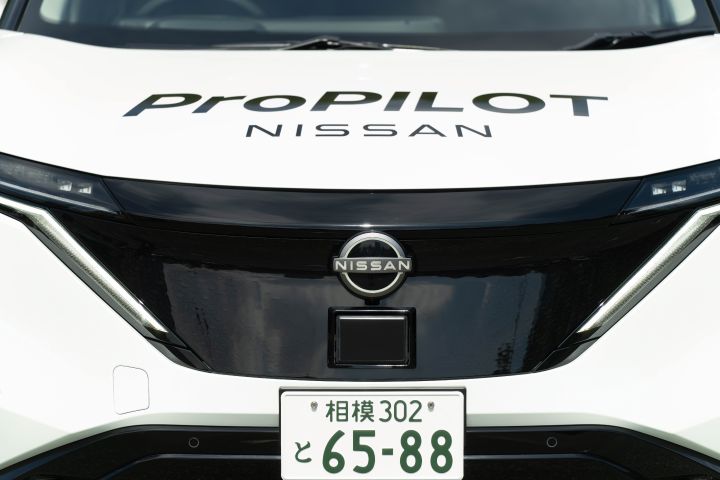 Der vordere Teil eines weißen Nissan Ariya ist mit der Front nach vorne gerichtet zu sehen, auf der Motorhaube ist die Aufschrift „ProPILOT NISSAN” zu erkennen.