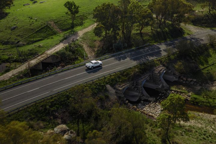 2026 Nissan Navara SL dual cab ute finished in Alpine White photographed from a drone above a roadside bridge and culvert crossing in farmland.