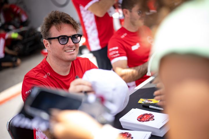 Oliver Rowland lächelt und gibt einem Fan in der Boxengasse seine signierte Kappe zurück.