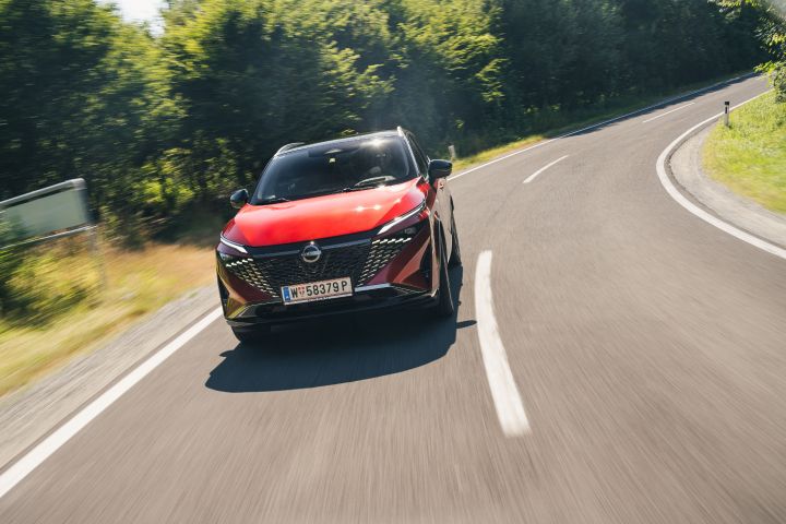 Frontale Fahraufnahme eines Nissan Qashqai in Fuji Sunset Red in einer sonnigen Landstraßenkurve