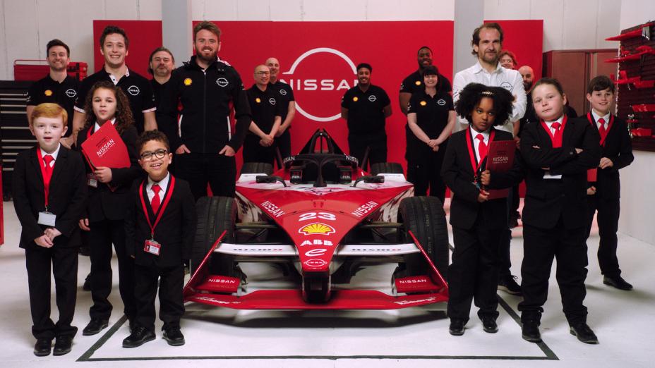 Crianças vestidas de terno e equipe da Nissan posam para foto de grupo com um carro de Fórmula E ao centro