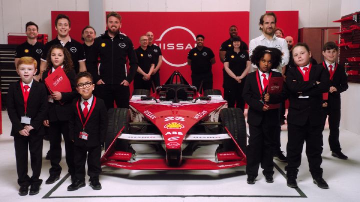 Crianças vestidas de terno e equipe da Nissan posam para foto de grupo com um carro de Fórmula E ao centro