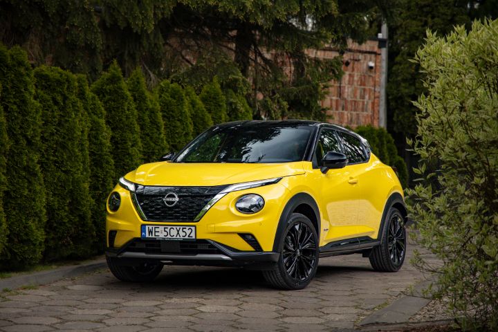 Żółty Nissan Juke stojący bokiem na tle budynku i drzew
