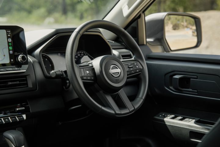 2026 Nissan Navara SL dual cab ute finished in Alpine White shown from the driver-side interior angle, featuring the steering wheel, gauge cluster, door panel and right-hand-drive layout.