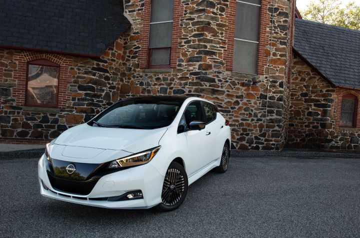 Front left 3/4 view of a white 2025 Nissan LEAF parked outside a warm-toned stone building.