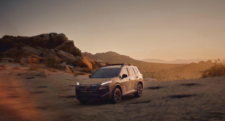 A Nissan Rogue Rock Creek driving on a cliff with dust in the air at sunset.