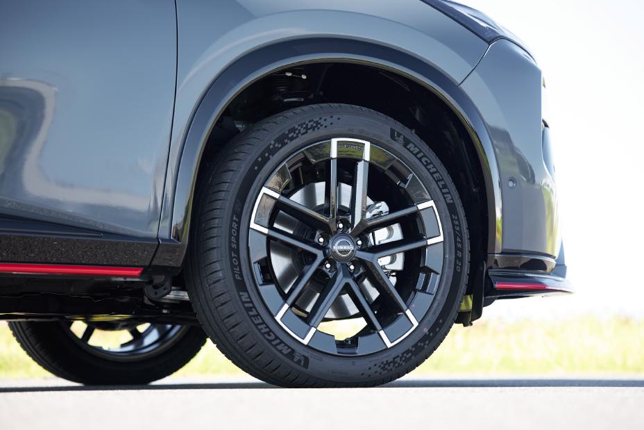 Close-up of the front wheel of a grey Nissan X-Trail NISMO. The wheel features a modern multi-spoke design with black and silver accents, and the tire is mounted. Part of the vehicle’s body is visible above the wheel.