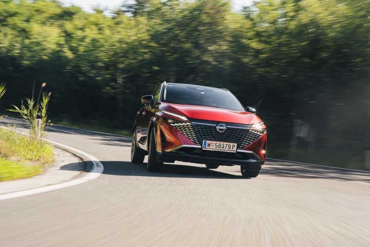 Ein Nissan Qashqai in Fuji Sunset Red fährt zügig durch eine Landstraßenkurve, Blick von vorne unten auf das Fahrzeug