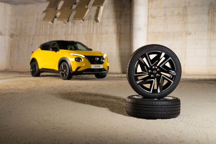 Gelber Nissan Juke 3/4 Front auf hellem Untergrund im Hintergrund und davor zwei Reifen mit silbernen Leichtmetallfelgen