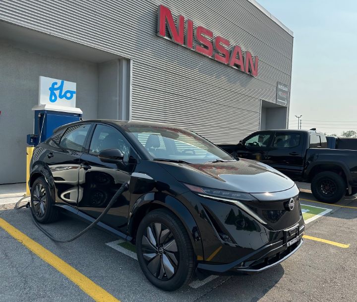 A black Nissan vehicle parked in front of a Nissan dealership.