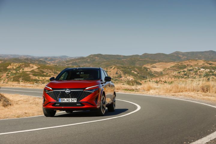 Nieuwe Nissan Qashqai in de kleur Fuji Sunset Red, van de voorzijde gezien, rijdend op een bochtige weg