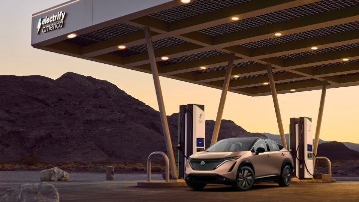 A Nissan Ariya parked under a charging station pavilion during sunset.
