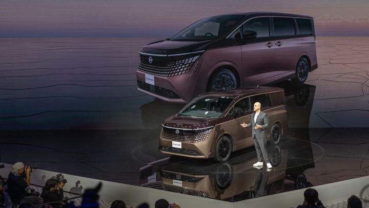 On the stage, the all-new Elgrand in Fuji Dawn and Shigoku two-tone colors is positioned diagonally, facing slightly to the left. Next to the vehicle stands CEO Ivan Espinosa in a suit, delivering a presentation.