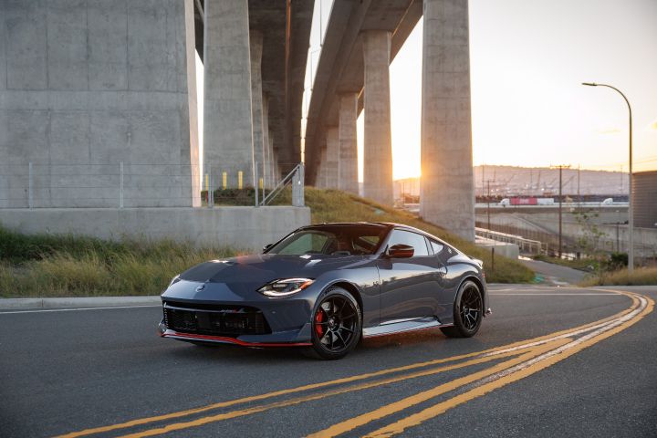 Front left 3/4 view of the 2027 Nissan Z NISMO MT curving under a highway bridge at sunset.