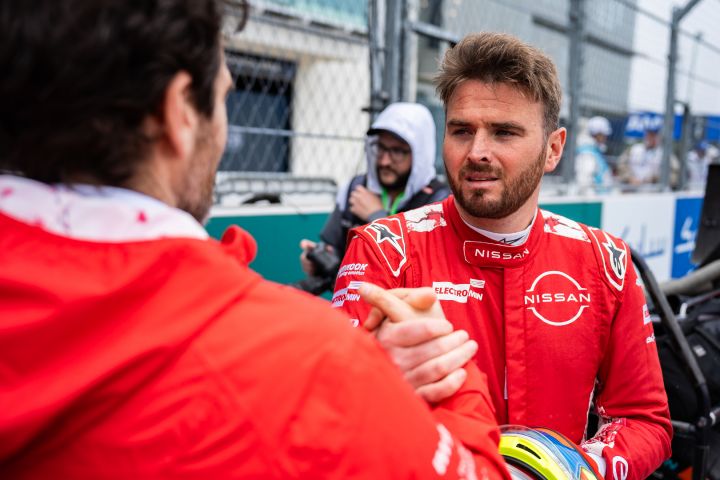 Oliver Rowland in seinem roten Rennanzug des Nissan Formula E Teams schüttelt vor dem Miami E-Prix dem Geschäftsführer und Teamchef des Nissan Formula E Teams, Tommaso Volpe, die Hand.