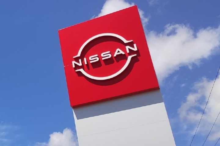 Placa de concessionária vermelha com o logo da Nissan e céu azul ao fundo
