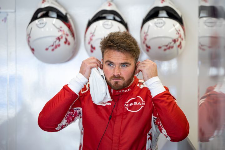 Oliver Rowland setzt sich vor einer Trainingssitzung in der Box seine Ohrhörer ein, während er seinen roten Rennanzug des Nissan Formula E Teams trägt.