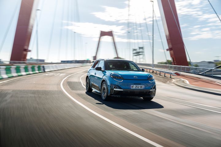 Ein blauer Nissan Micra fährt über eine Brücke in Rotterdam, die wegen der Geschwindigkeit nur unscharf im Hintergrund zu sehen ist
