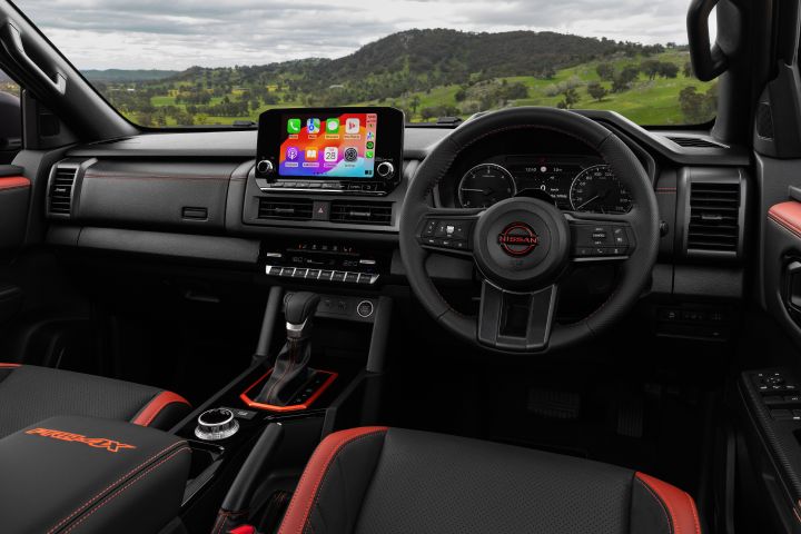 2026 Nissan Navara PRO-4X finished in Boulder Grey featuring the interior overview with Apple CarPlay on the infotainment screen and red-trimmed seating.