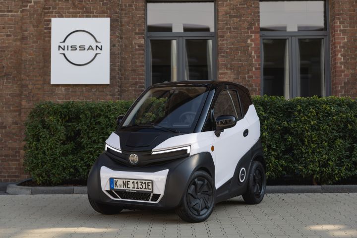 Das schwarz-weiße Nanocar S04 steht vor dem Nissan Deutschland Gebäude mit roter Backsteinfront und grüner Hecke