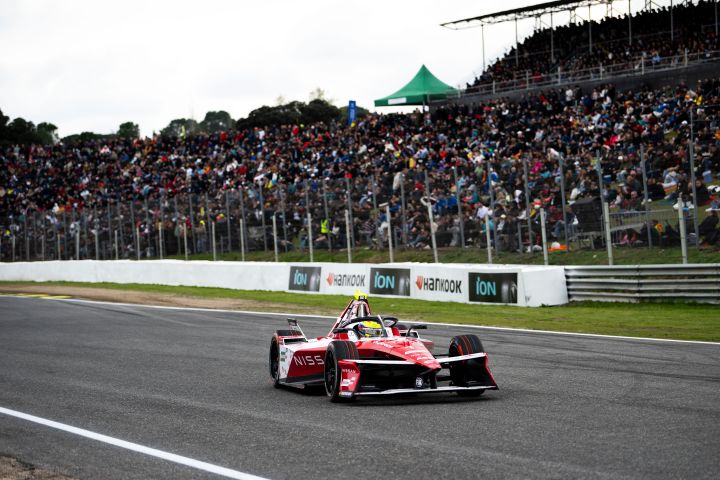 Frontalaufnahme von Oliver Rowland während des E-Prix von Madrid auf der Rennstrecke im Auto mit der Startnummer 1, hinter ihm die Fans.