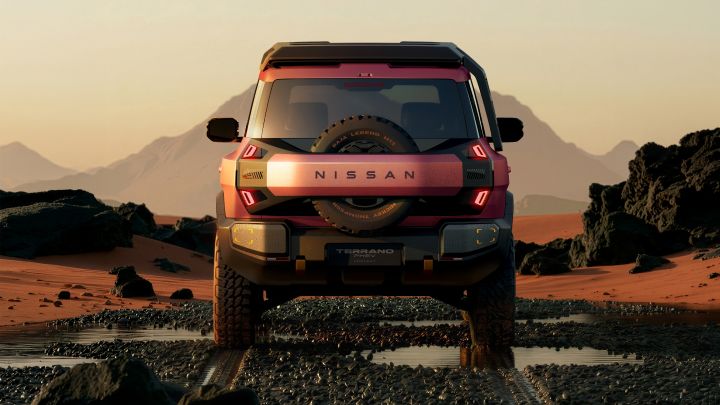 A red Terrano PHEV Concept driving toward the viewer in a desert at sunset. Rocky and sandy terrain surrounds the vehicle, with puddles in the foreground and distant mountains under a soft evening sky.