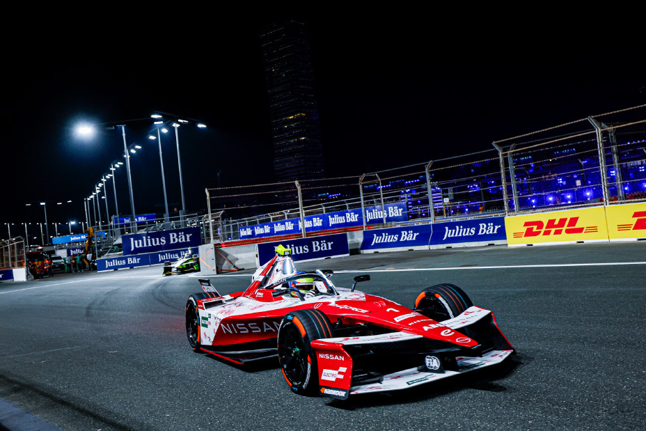 Front on shot of Oliver Rowland driving the #1 Nissan e‑4ORCE 05 in Jeddah with blue advertising boards visible behind the car.