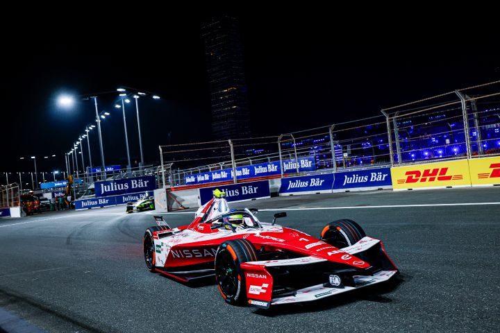 Front on shot of Oliver Rowland driving the #1 Nissan e‑4ORCE 05 in Jeddah with blue advertising boards visible behind the car.