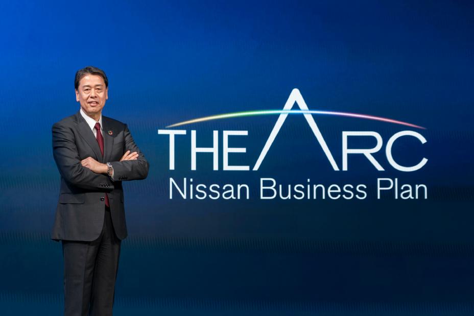 Makoto Uchida pose à côté du logo du nouveau plan à moyen terme de Nissan