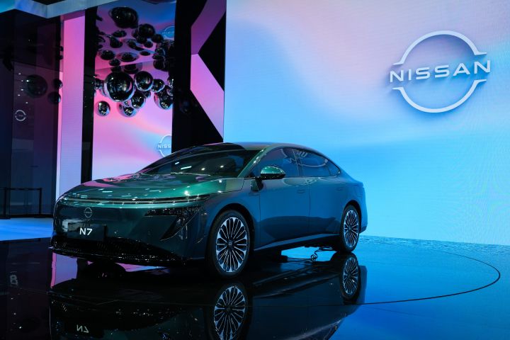 東風日産の緑色の新型セダン電気自動車「N7」低位置からの正面図。背後にパステルカラーの電子サインと日産ロゴ、天井から銀色のボールが下がっている。
