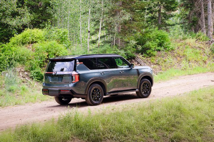 Right rear 3/4 view of a gray 2025 Nissan Armada on a dirt path in the woods on a sunny day.