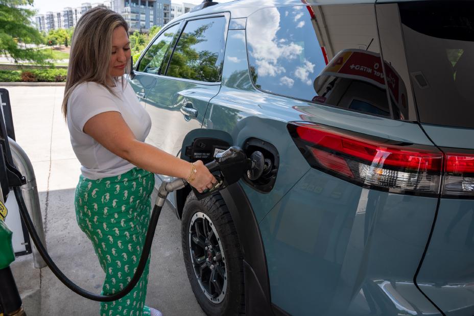 A woman putting gas into a Nissan SUV, she is holding onto the gas pump.
