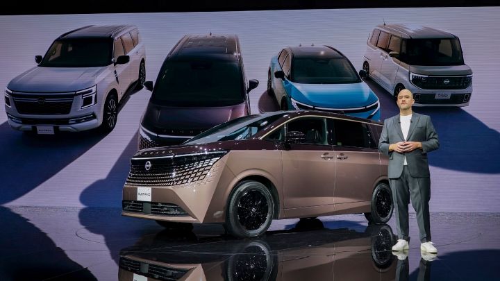 On the stage, the all-new Elgrand in Fuji Dawn and Shigoku two-tone colors is positioned diagonally, facing slightly to the left.  Next to the vehicle stands CEO Ivan Espinosa in a suit, with hands clasped in front. In the background, four models—Elgrand, Patrol, Nissan LEAF, and Roox—are displayed.