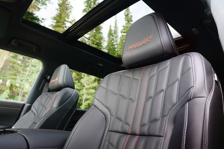 Angled close up of the black leather and red stitching front seats, you can see through the side windows and sunroof.