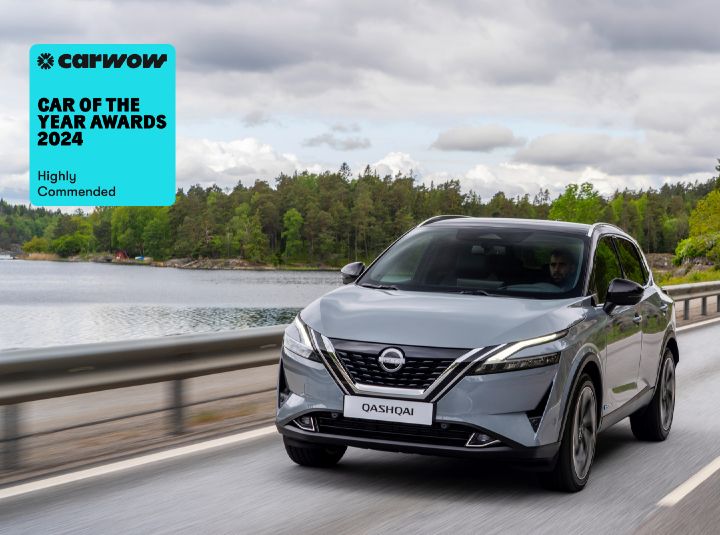 A grey Nissan Qashqai driving down a street beside a body of water