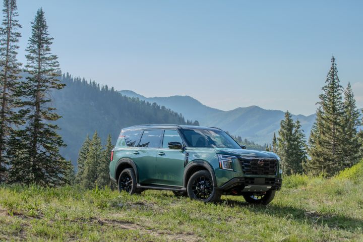 Front right 3/4 view of a 2025 Nissan Armada parked on a grassy hilltop overlooking pine tree scattered mountains.