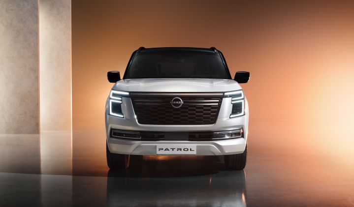 A white Patrol SUV is photographed from the rear, showcasing its refined design and modern taillights. The background is a minimalist space with vertically aligned light pillars.